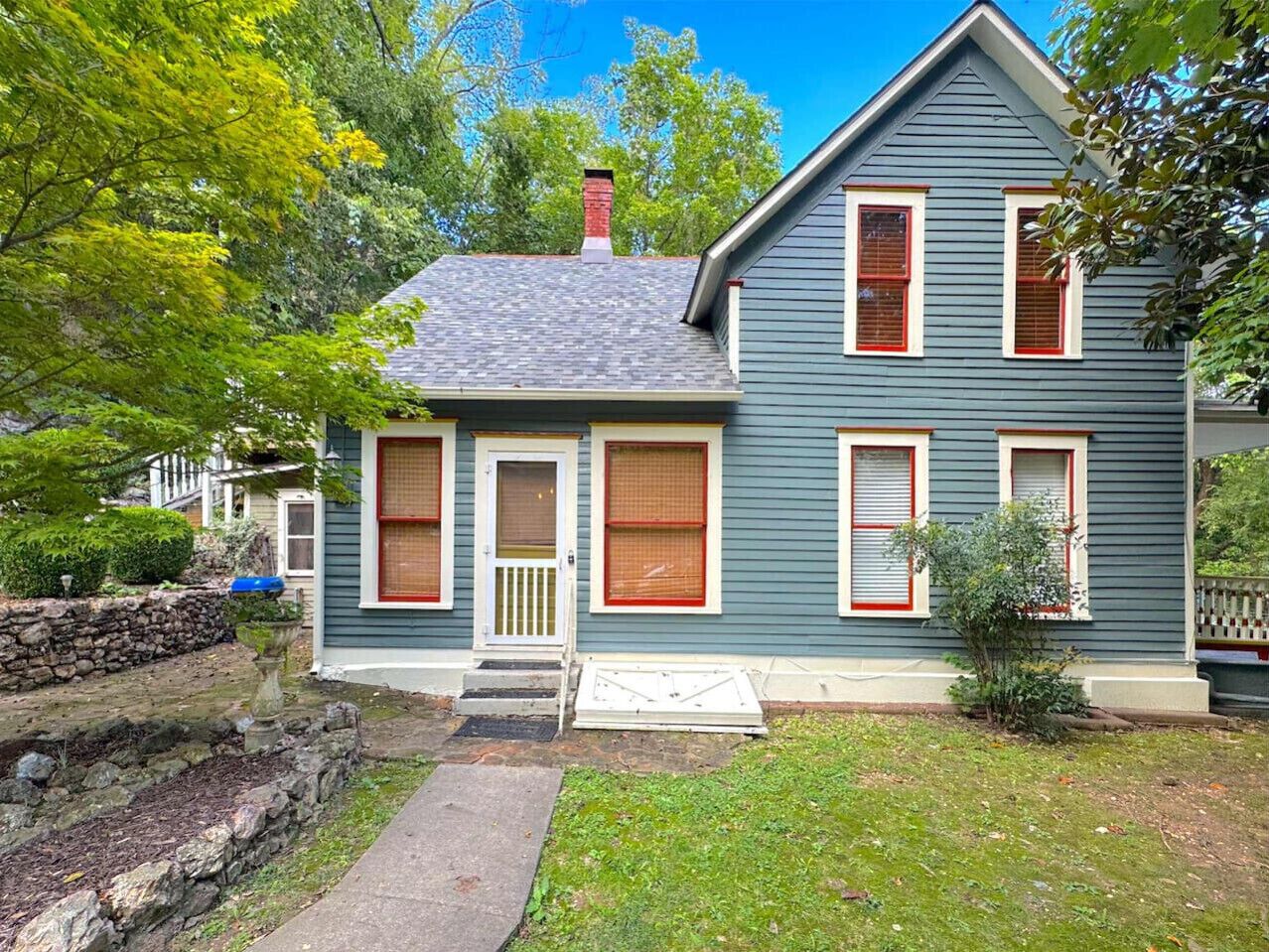 A two-story house with a front porch, a chimney, and a stone wall.