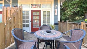 A patio with a round table and four wicker chairs, a wooden fence, and a building with a red door and a sign reading "66 Center Street Studio No. 2".