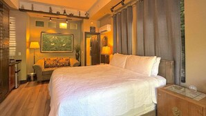 A hotel room with a large bed, a wooden nightstand, a desk, and a chair. - 66 Center - The Studio (Eureka Springs)