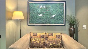 A room with a light blue wall, a framed painting of birds and foliage, a floor lamp, a sofa with patterned cushions, and a potted plant. - 66 Center - The Studio (Eureka Springs)