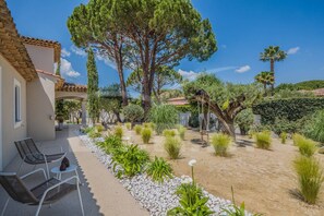 Une terrasse avec des sièges extérieurs, entourée d’un jardin où poussent différentes plantes et arbres.