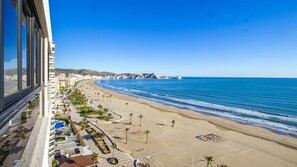 A coastal hotel with a beach view, a promenade, and a clear blue sky.