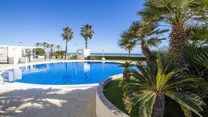 En swimmingpool med utsikt över havet, omgiven av palmer och en klar himmel.