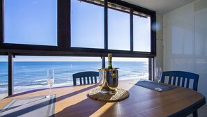 Ett matbord med en flaska champagne, två vinglas och utsikt över havet genom stora fönster.