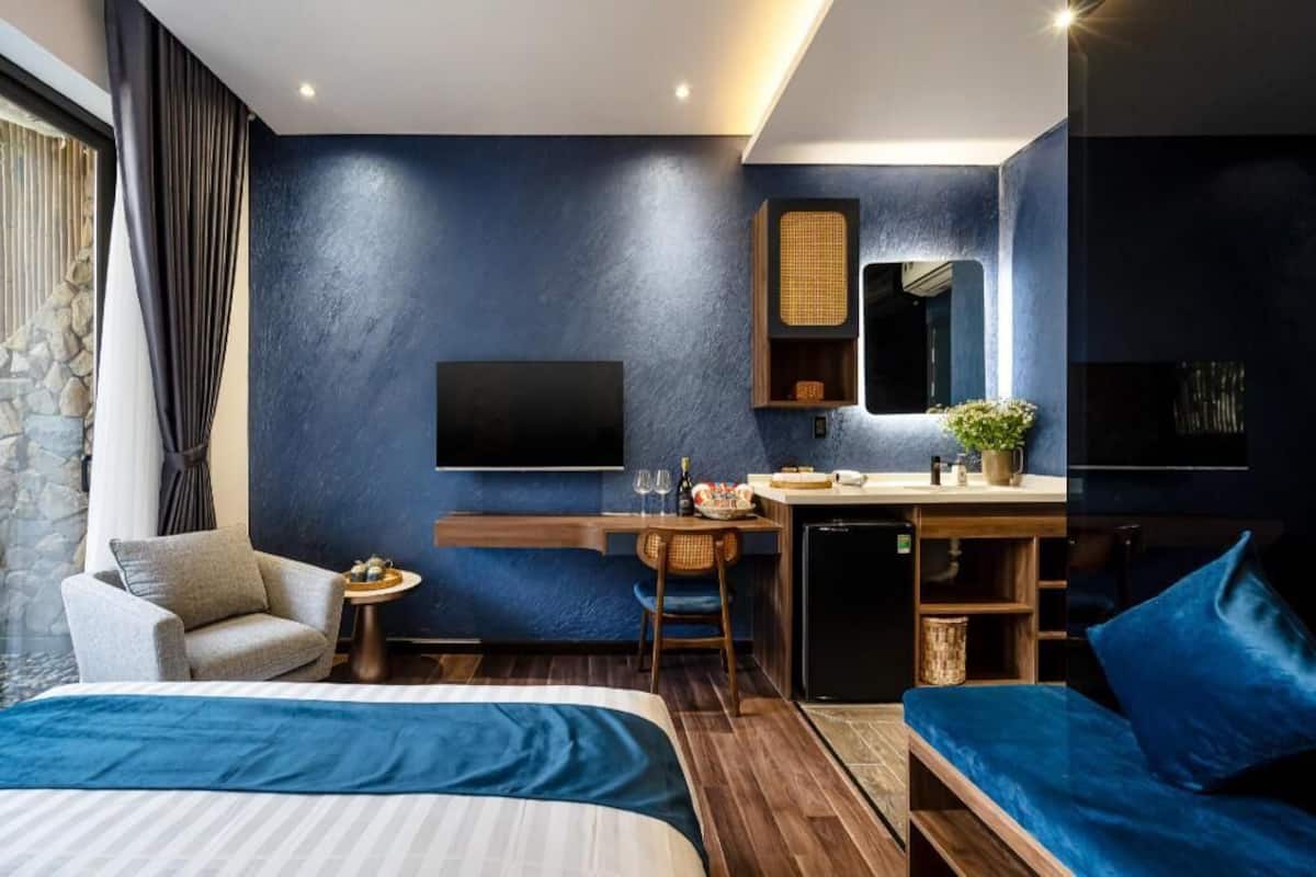 A modern hotel room with a large bed, a desk, a small fridge, a television, and a window with curtains.