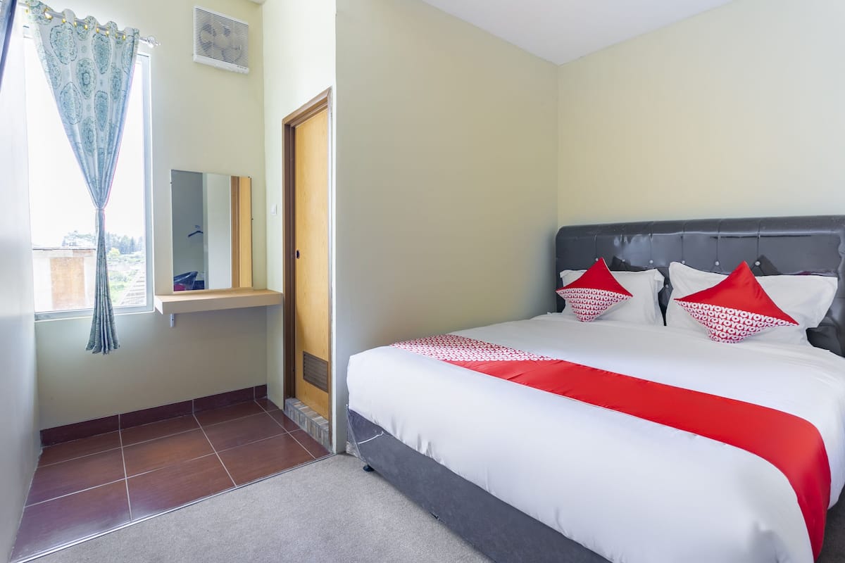 A bedroom with a bed, a mirror, and a window with curtains.