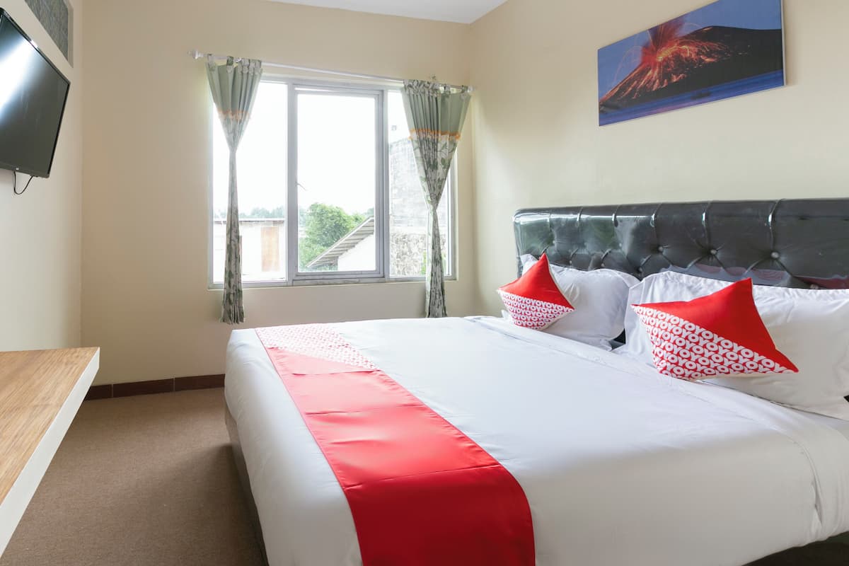 A hotel room with a bed, a TV, a window with curtains, and a painting on the wall.