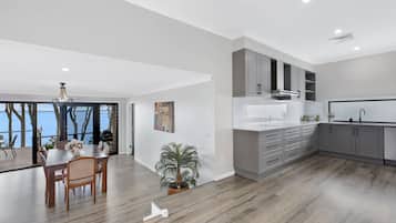 A modern kitchen with grey cabinets, a white countertop, and a built-in oven. There is a dining area with a wooden table and chairs, and a potted plant.