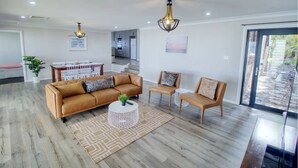 En moderne stue med sofa, lænestole og sofabord. Der er et spiseområde med bord og stole. Værelset har et stort vindue og udsigt ud.
