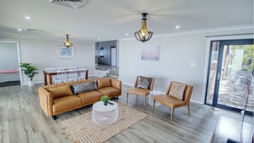 A modern living room with a sofa, chairs, and a coffee table. There is a dining area with a table and chairs. The room has a large window and a view of the outside.