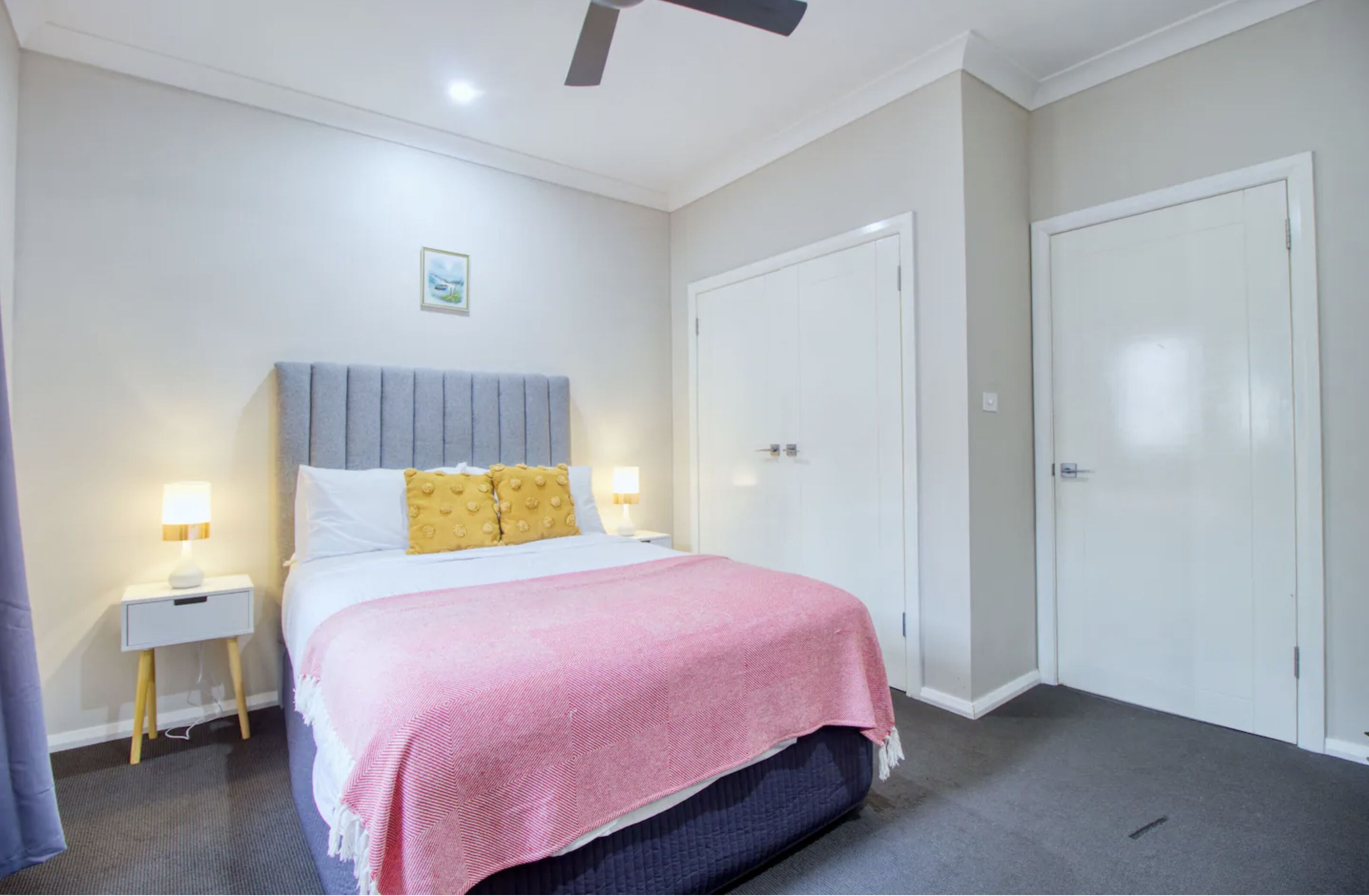 A bedroom with a bed, two bedside tables with lamps, a ceiling fan, and a wardrobe.