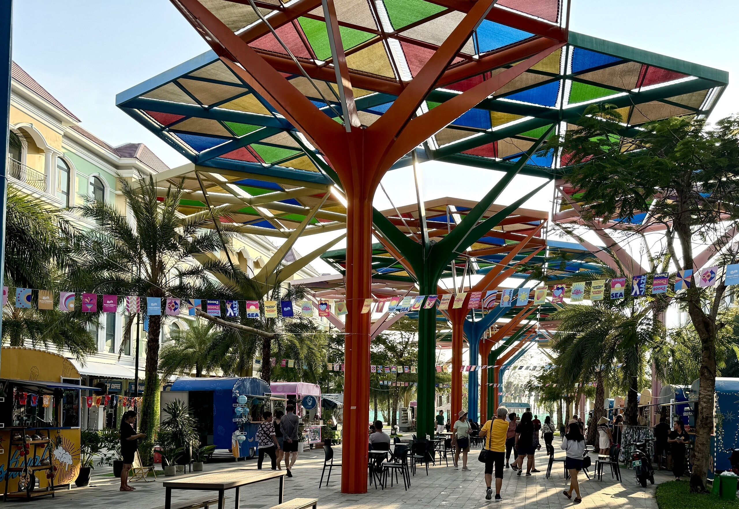 Un mercado al aire libre con toldos coloridos, palmeras y varios puestos.