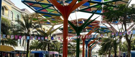 Un mercado al aire libre con toldos coloridos, palmeras y varios puestos.