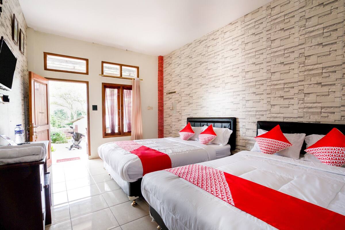 A hotel room with two beds, a brick wall, and a view of the outdoors.