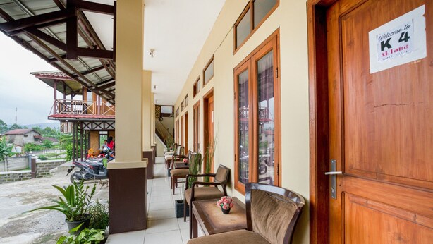 A hotel entrance with a wooden door, a sign reading "Welcome to K4 Alanta," and a covered outdoor seating area with chairs and potted plants.