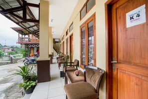 L’entrée d’un hôtel, avec une porte en bois, une enseigne indiquant « Bienvenue à l’hôtel K4 Alanta », et un espace extérieur abrité avec des chaises et des plantes en pot.