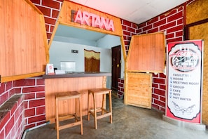 A restaurant interior with a wooden counter, stools, and a sign listing amenities like room, meeting room, cafe, group, wifi, and hot water. - Super OYO 2961 Artana Bed & Breakfast (Pangalengan)
