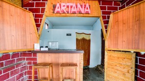 A rustic wooden interior with a reception desk, two stools, and a sign that reads "ARTANA".