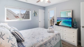 Une chambre à coucher avec un lit, un ventilateur de plafond, une télévision et une fenêtre donnant sur le ciel.