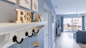 Un intérieur moderne avec une cheminée, des lettres en bois formant le mot « RELAX » au-dessus, et une vue sur un espace de vie comprenant un canapé et une table à manger.