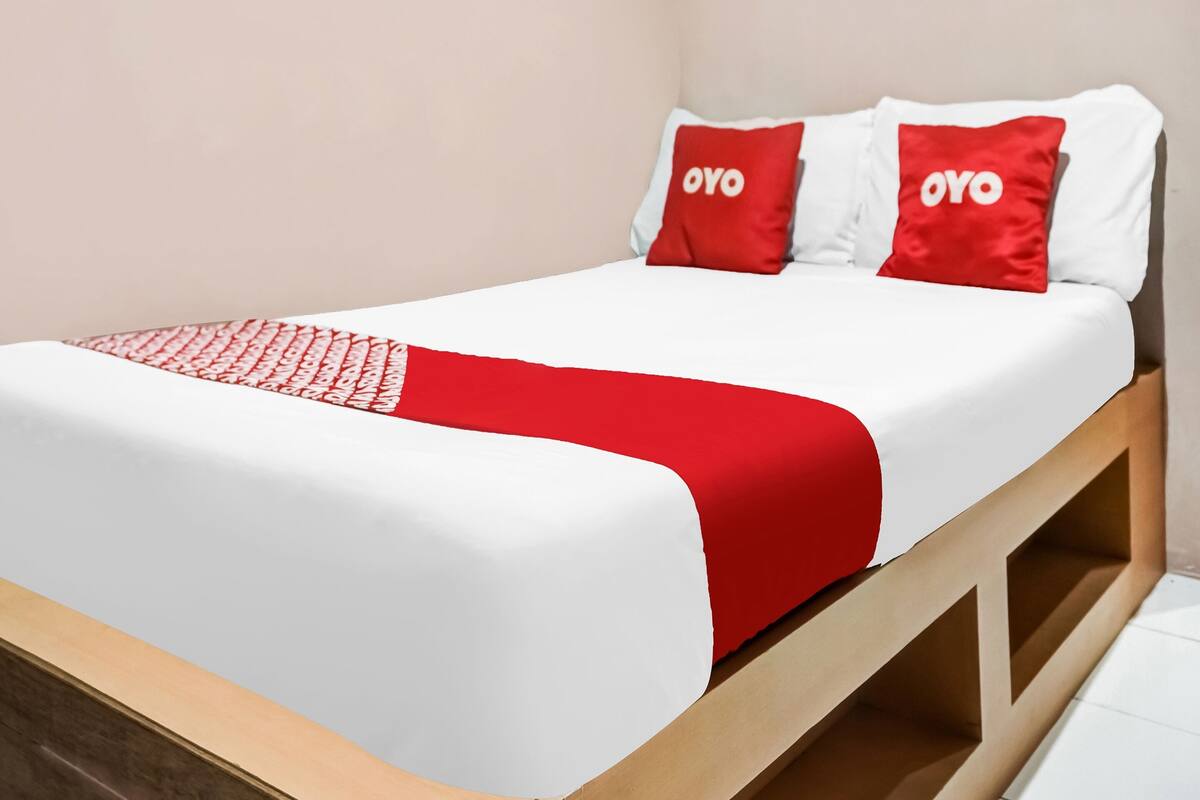 A bed with white and red bedding, two red pillows with "OYO" text, and a wooden headboard.