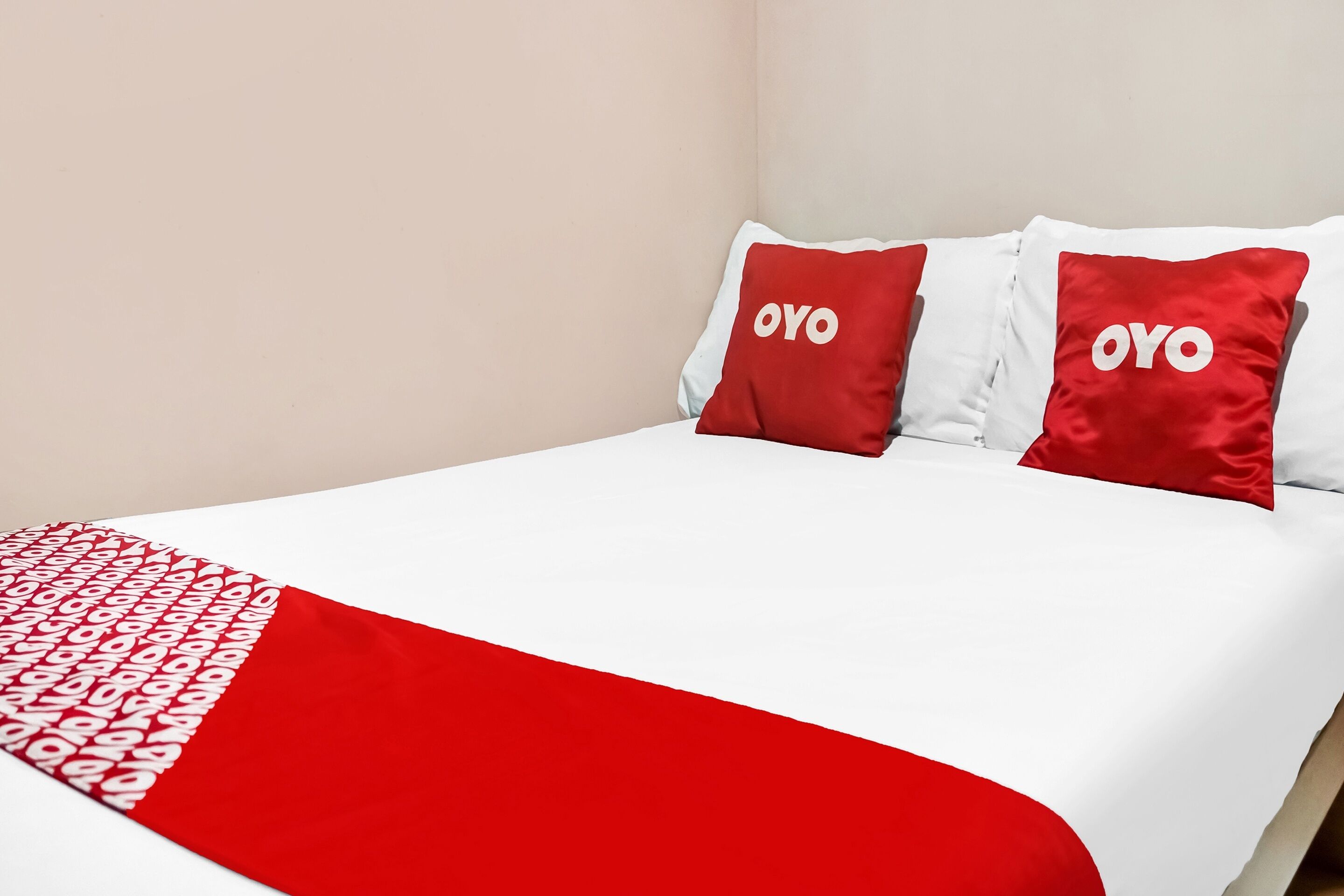 A bed with a white and red bedspread, two pillows with the word "OYO" on them, and a red and white blanket.