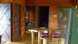 Un intérieur rustique avec des murs et des planchers en bois, une table en bois, deux chaises et un réfrigérateur vert.