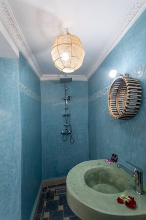 A bathroom with a blue wall, a round sink, a shower with a metal hose, and a hanging light fixture. - RIAD MALAYINE (Marrakech)