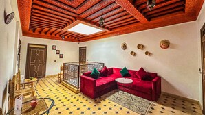 A room with a red sofa, a small round table, and a patterned floor. - RIAD MALAYINE (Marrakech)