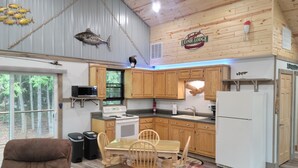 A cozy cabin interior with a dining area, kitchen, and a large window overlooking the forest.