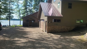 A two-story lodge with a metal roof, a gravel driveway, and a view of a lake.