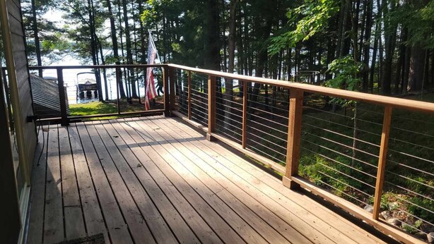 A wooden deck with a metal railing overlooking a forested area.