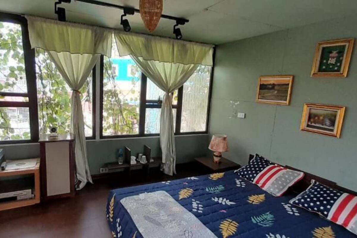 A room with a bed, a desk, and a window with curtains. There are framed pictures on the wall.