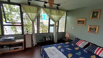 Una habitación con una cama, un escritorio y un ventanal con cortinas. En la pared hay cuadros enmarcados.
