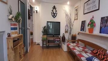 A cozy living room with a wooden floor, a sofa, a TV, and a bookshelf.