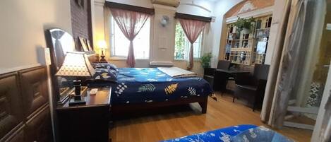 A bedroom with a bed, bedside table, lamp, and a desk with a chair.