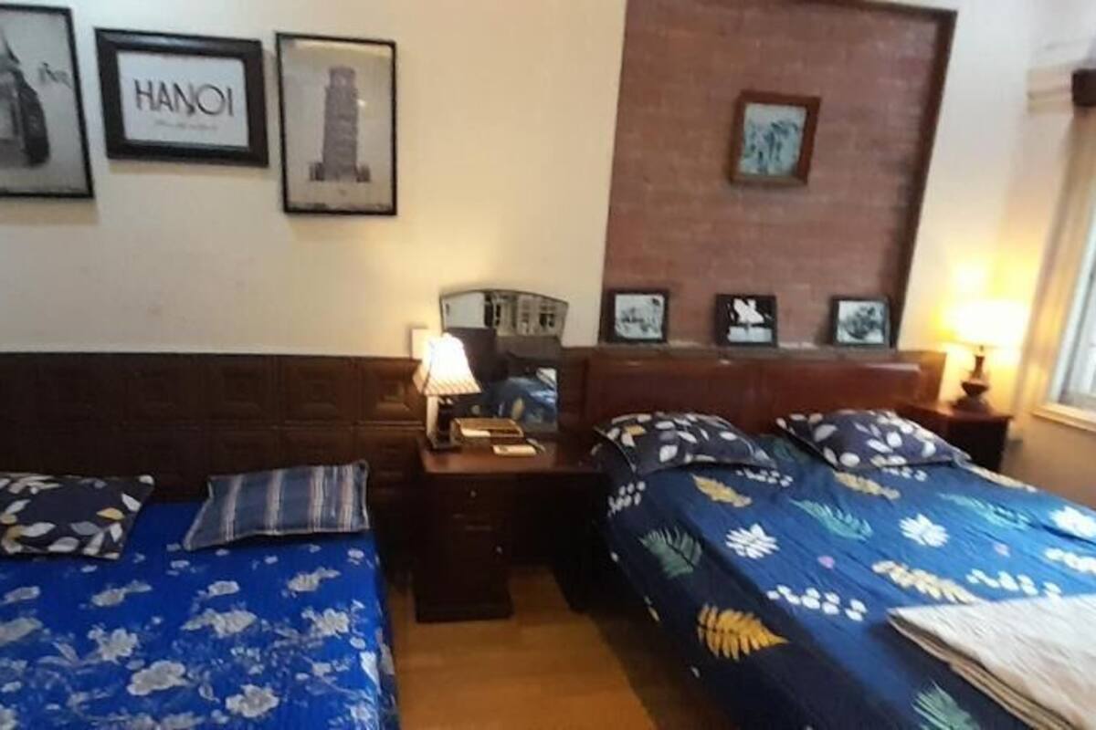 A hotel room with two beds, a nightstand, a lamp, and framed pictures on the wall.