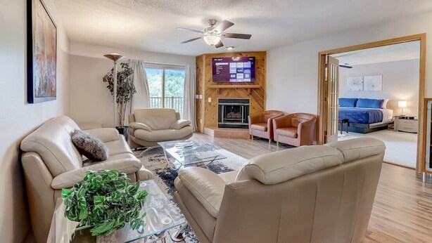A spacious living room with a fireplace, leather sofas, a glass coffee table, and a ceiling fan. - Josie's On The Bay - Waterfront, Fireplace, Roku (Wisconsin Dells)