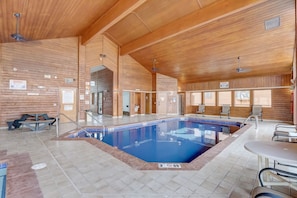 Ein großer Innenpool mit Holzwänden und -decke, umgeben von Sitzbereichen und einem kleinen Tisch.