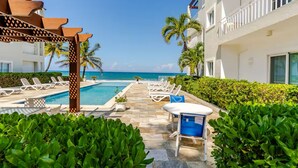 A poolside area with lounge chairs and a pergola, overlooking a beach and ocean. - Refurbished BeachFront Penthouse - Music themed! (Cabarete)