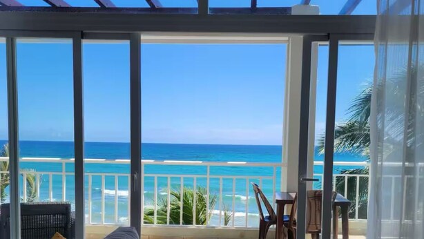 A room with a large glass door leading to a balcony with a view of the ocean. - Refurbished BeachFront Penthouse - Music themed! (Cabarete)
