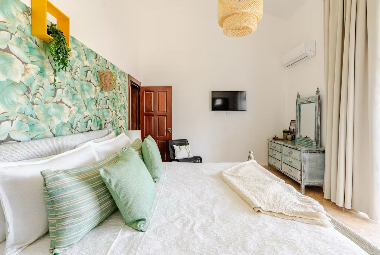 A bedroom with a bed, pillows, a dresser, a television, and a wall-mounted air conditioner.