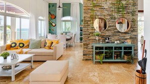 A modern living room with a stone wall, a round mirror, and a green console table. - Refurbished BeachFront Penthouse - Music themed! (Cabarete)