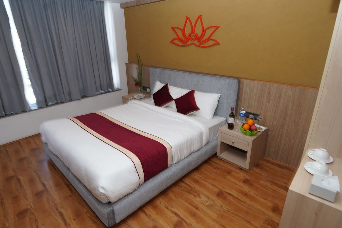A neatly made bed with a red and white bedspread, a wooden nightstand with a bottle and fruit, and a wall-mounted red lotus symbol.