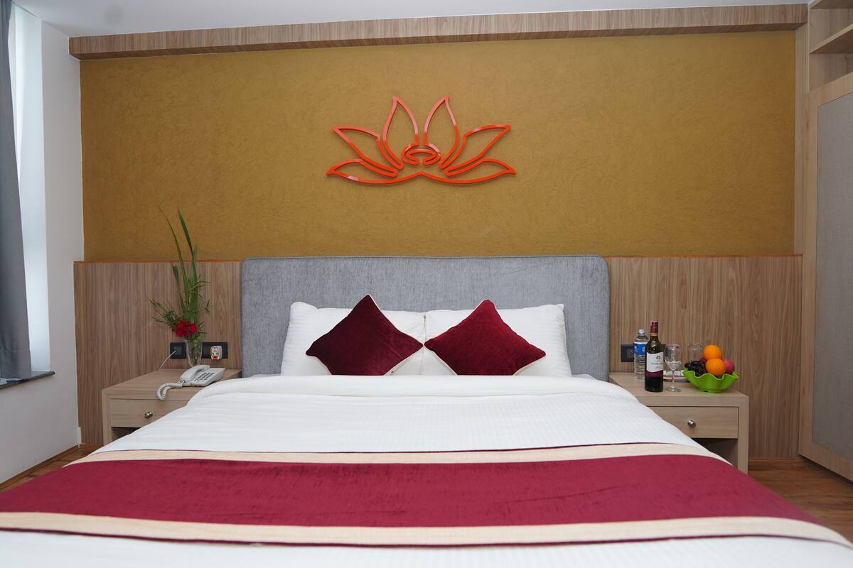 A hotel room with a bed, a nightstand, a wall-mounted phone, a decorative wall piece, and a fruit bowl.