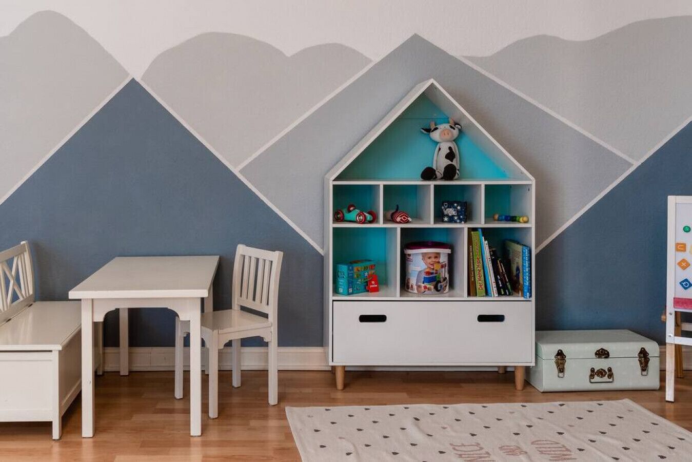 Une chambre d’enfant avec un bureau blanc, des chaises, une bibliothèque et un espace de jeux.