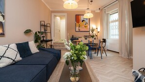 Un salon moderne avec un canapé bleu foncé, une table basse ornée d’un vase de fleurs, un coin repas avec des chaises et, au fond, une cuisine.