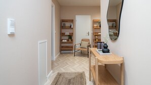 Un couloir doté d’un plancher en bois, d’une chaise, d’une console sur laquelle est posé un vase, ainsi que d’étagères remplies de livres et d’objets décoratifs.