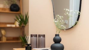 Une table en bois ornée d’un vase et de bougies, un miroir accroché au mur et une étagère avec des plantes et des objets décoratifs.