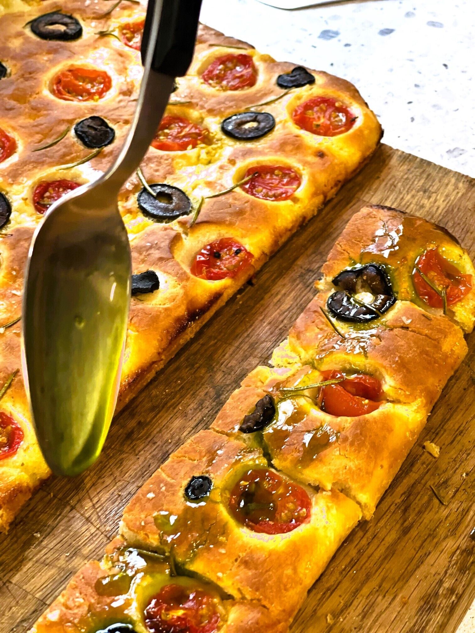 A pizza with black olives and red tomatoes on a wooden cutting board.